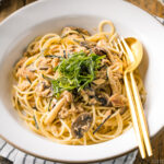 A white ceramic plate containing Japanese-style Tuna Mushroom Pasta garnished with shredded nori and shiso leaves.