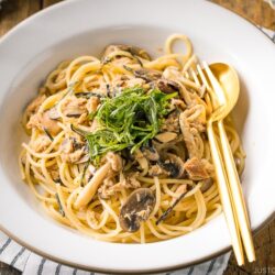 A white ceramic plate containing Japanese-style Tuna Mushroom Pasta garnished with shredded nori and shiso leaves.