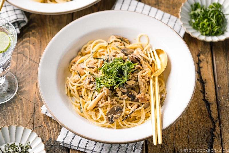 A white ceramic plate containing Japanese-style Tuna Mushroom Pasta garnished with shredded nori and shiso leaves.