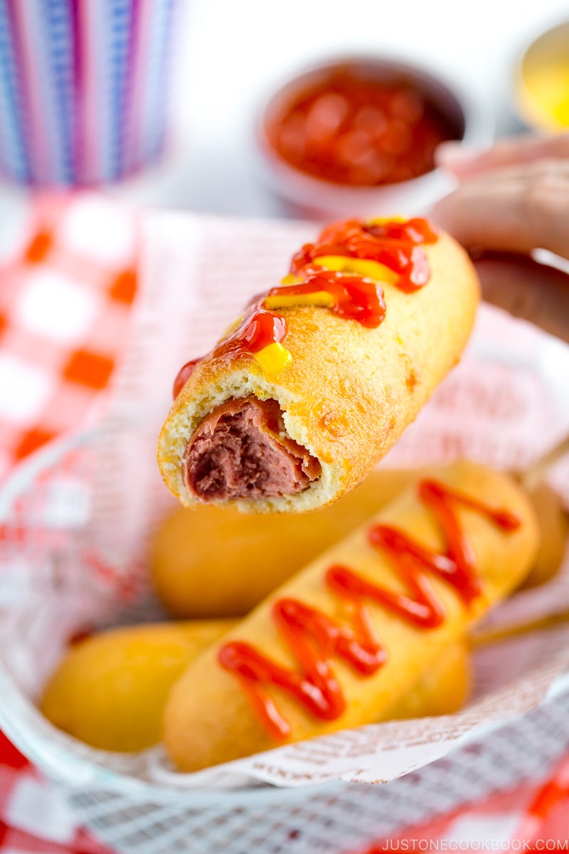 A basket containing corn dogs served with ketchup and mustard drizzle.