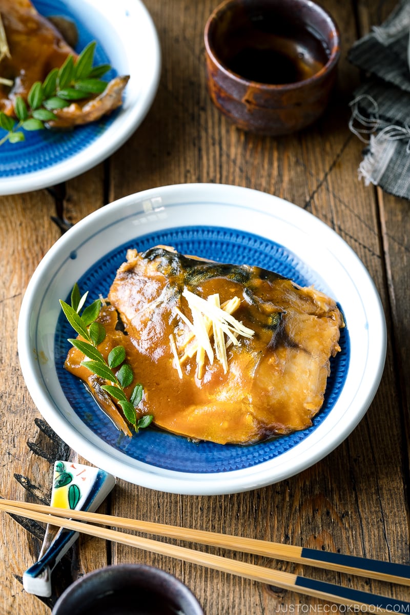 A blue Japanese plate containing Saba Misoni (Mackerel Simmered in Miso) garnished with julienned ginger.