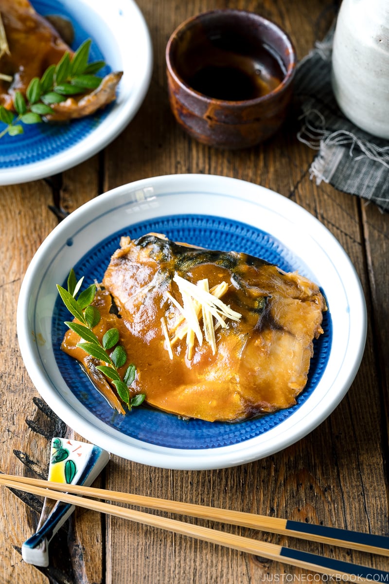 A blue Japanese plate containing Saba Misoni (Mackerel Simmered in Miso) garnished with julienned ginger.