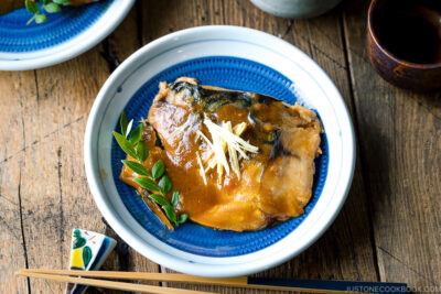 A blue Japanese plate containing Saba Misoni (Mackerel Simmered in Miso) garnished with julienned ginger.