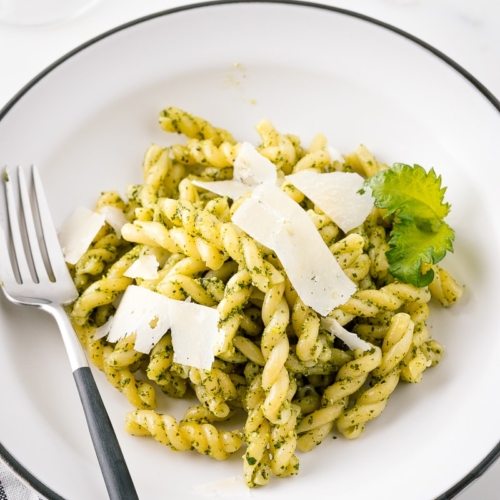 A white bowl containing Shiso Pesto Pasta garnished with shaved Parmesan cheese and shiso leaves.