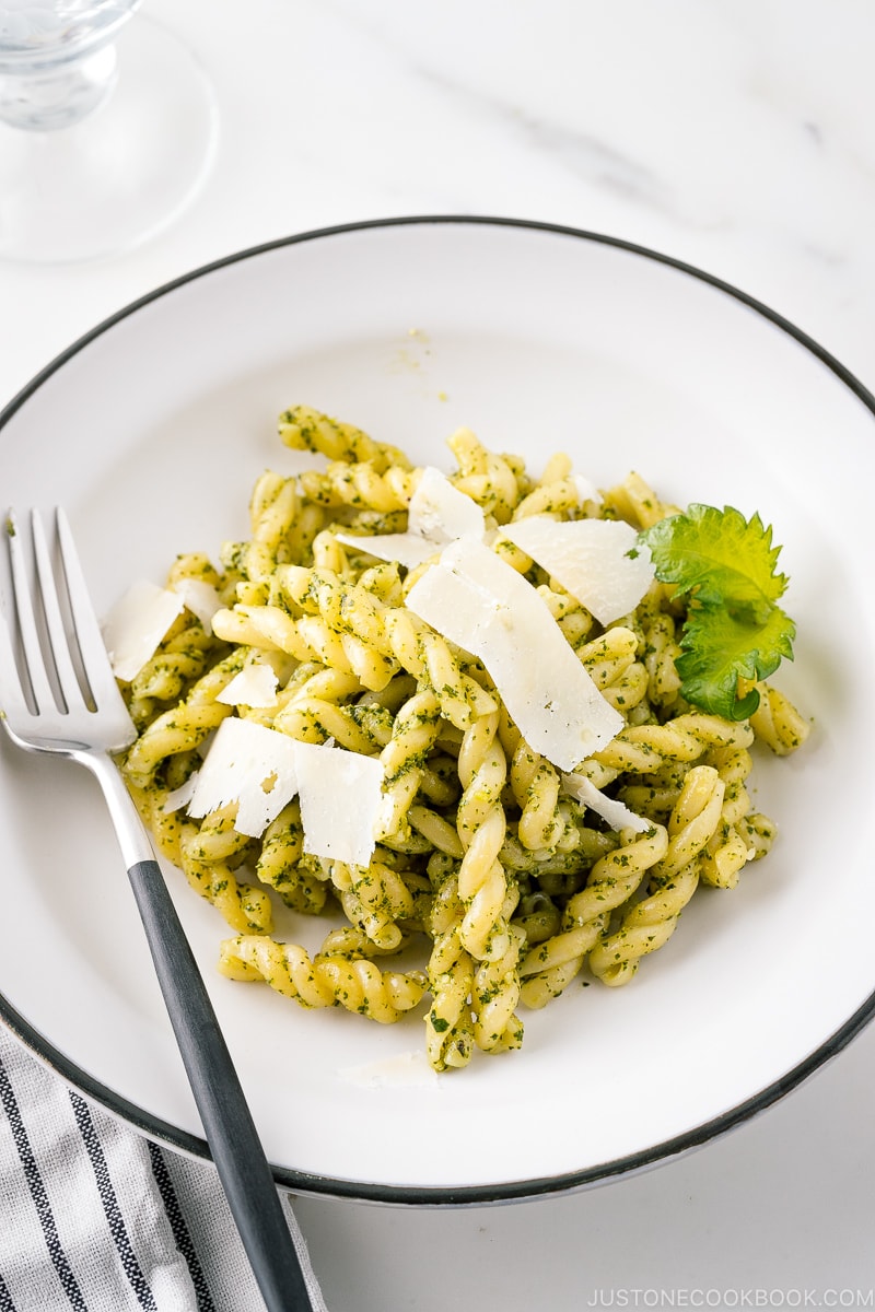 A white bowl containing Shiso Pesto Pasta garnished with shaved Parmesan cheese and shiso leaves.