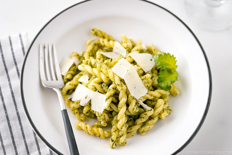 A white bowl containing Shiso Pesto Pasta garnished with shaved Parmesan cheese and shiso leaves.