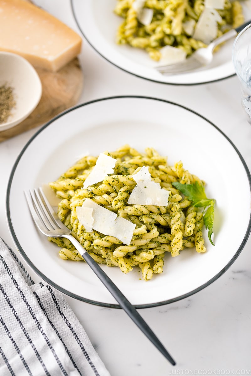 A white bowl containing Shiso Pesto Pasta garnished with shaved Parmesan cheese and shiso leaves.