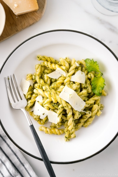 A white bowl containing Shiso Pesto Pasta garnished with shaved Parmesan cheese and shiso leaves.