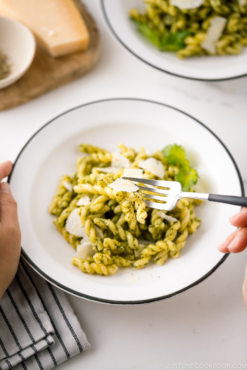 A white bowl containing Shiso Pesto Pasta garnished with shaved Parmesan cheese and shiso leaves.