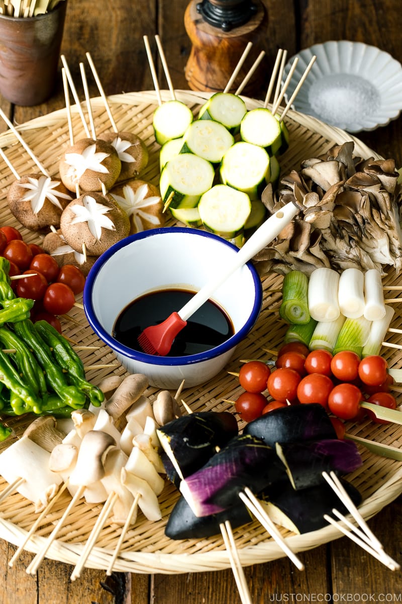 A bamboo basket containing various vegetables and mushrooms in skewers.