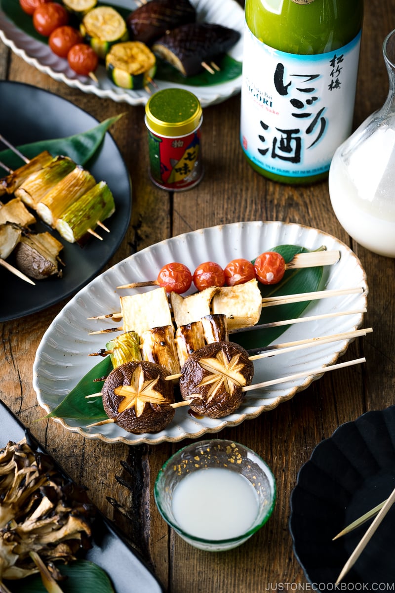 A ceramic plate containing Yakitori Style Grilled Vegetables along with Nigori Sake.