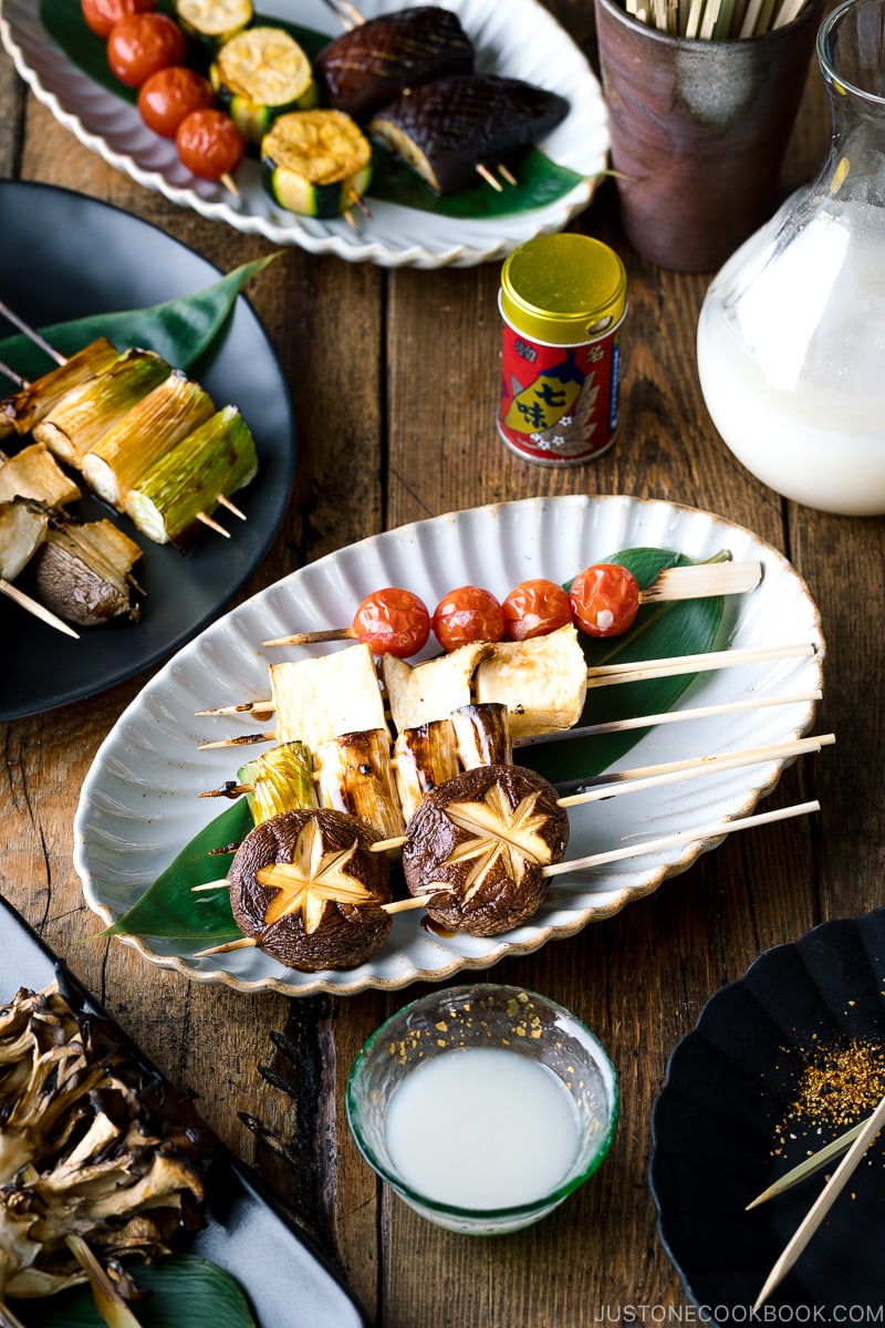 A ceramic plate containing Yakitori Style Grilled Vegetables along with Nigori Sake.