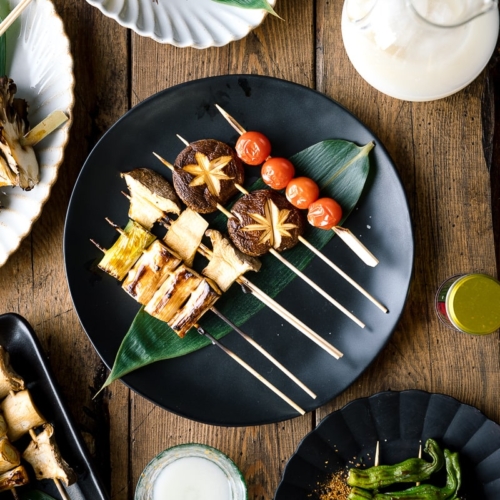 A ceramic plate containing Yakitori Style Grilled Vegetables along with Nigori Sake.