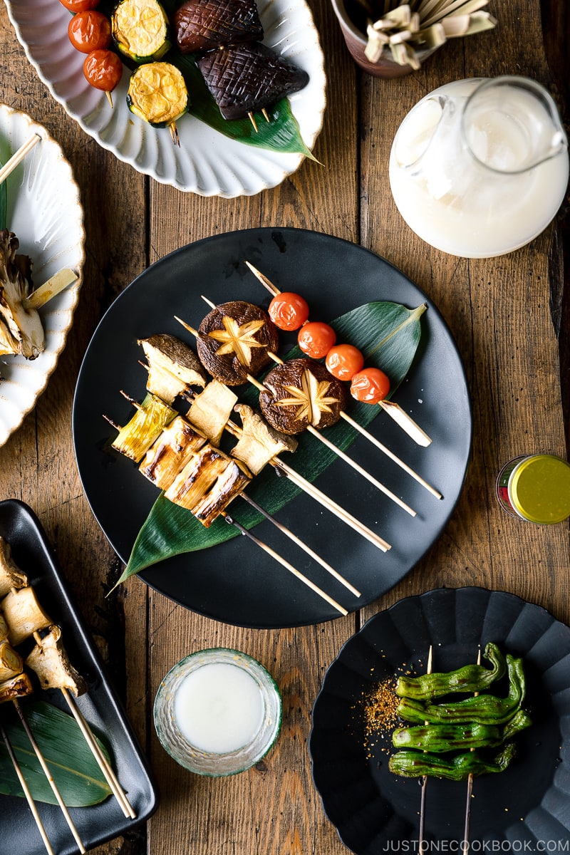 A ceramic plate containing Yakitori Style Grilled Vegetables along with Nigori Sake.