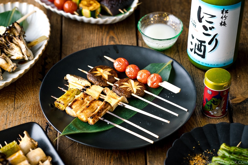 A ceramic plate containing Yakitori Style Grilled Vegetables along with Nigori Sake.
