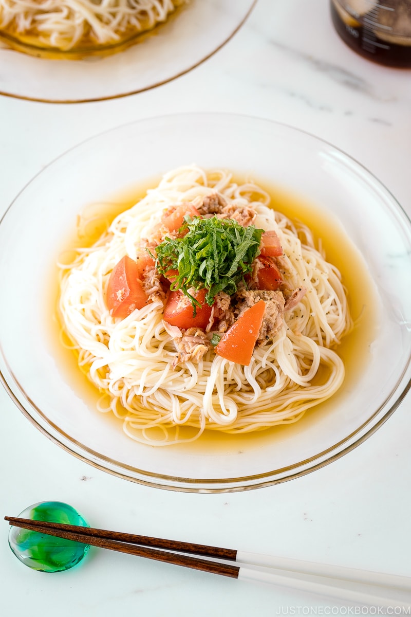 A glass plate containing Cold Tuna Tomato Somen topped with julienned shiso leaves.