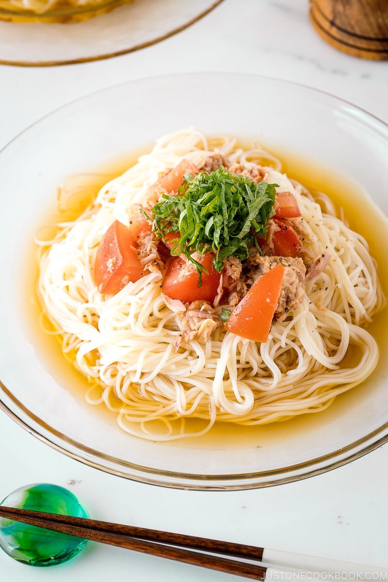 Une assiette en verre contenant du Somen froid au thon et à la tomate garni de feuilles de shiso en julienne.