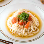 A glass plate containing Cold Tuna Tomato Somen topped with julienned shiso leaves.