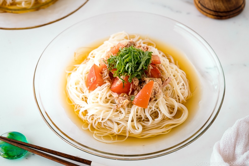 A glass plate containing Cold Tuna Tomato Somen topped with julienned shiso leaves.