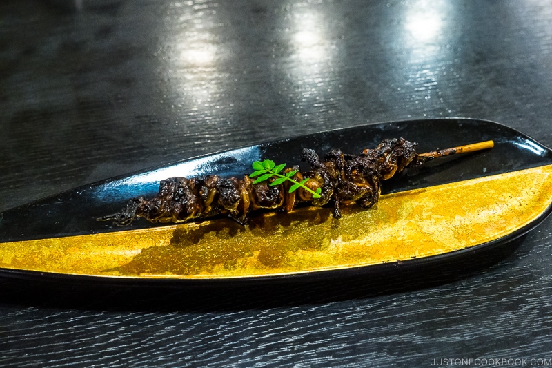grilled eel intestine on a skewer on a black and gold plate