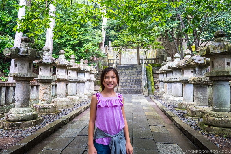 a girl standing on a stone path with stone lanterns on the side