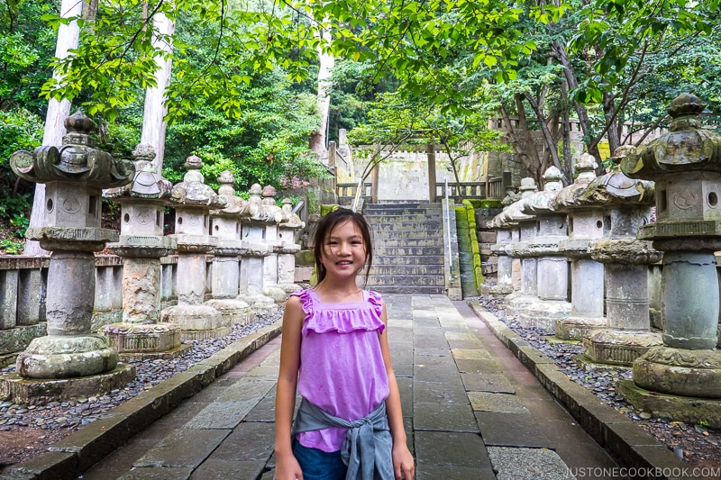 a girl standing on a stone path with stone lanterns on the side