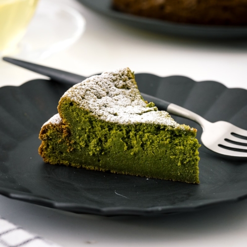 A black plate containing a slice of Matcha Gateau au Chocolat dusted with powdered sugar.