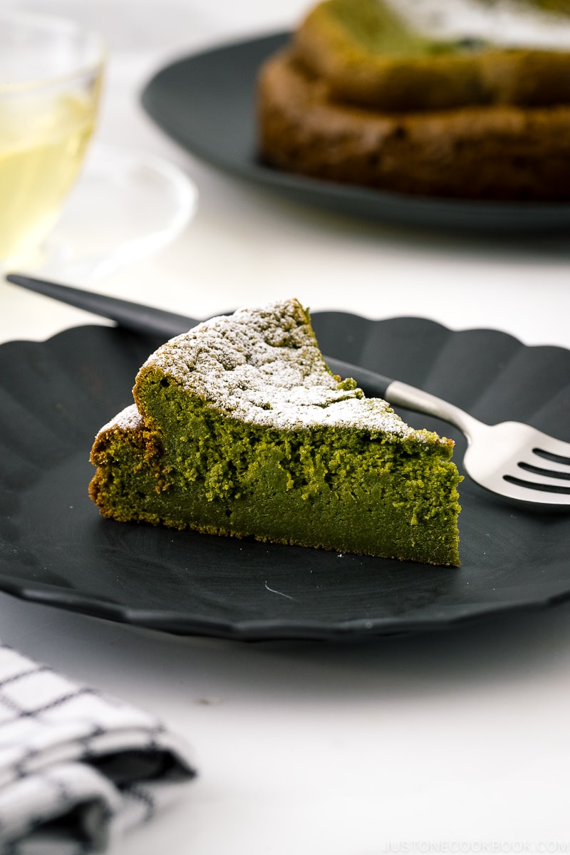 A black plate containing a slice of Matcha Gateau au Chocolat dusted with powdered sugar.