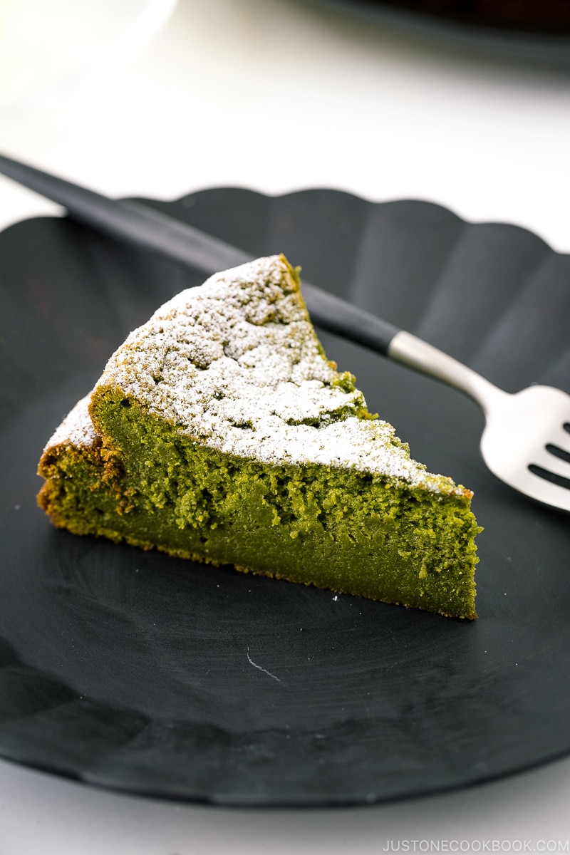 A black plate containing a slice of Matcha Gateau au Chocolat dusted with powdered sugar.