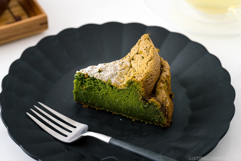 A black plate containing a slice of Matcha Gateau au Chocolat dusted with powdered sugar.