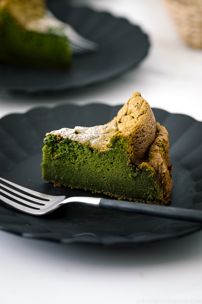 A black plate containing a slice of Matcha Gateau au Chocolat dusted with powdered sugar.