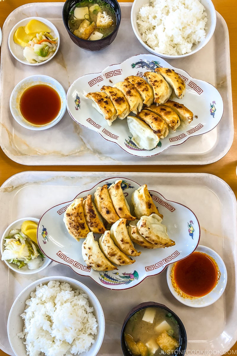 two trays containing gyoza on a plate next to rice soup and pickles