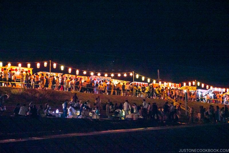 people walking along a riverbank festival at night