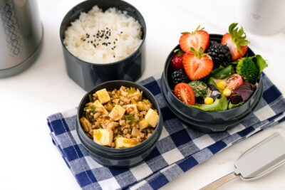 A Zojirushi lunch jar containing steamed rice, mapo tofu, fruits, and salad.