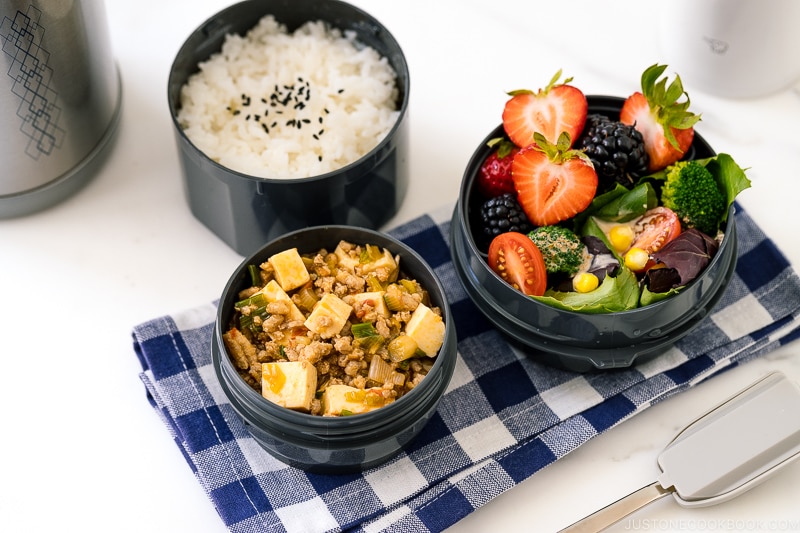 A Zojirushi lunch jar containing steamed rice, mapo tofu, fruits, and salad.