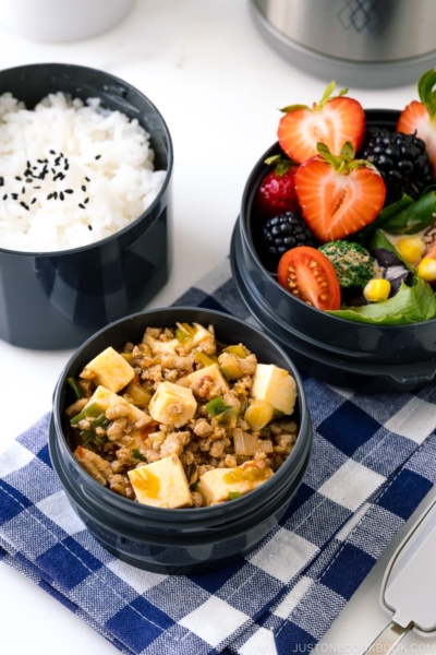 A Zojirushi lunch jar containing steamed rice, mapo tofu, fruits, and salad.