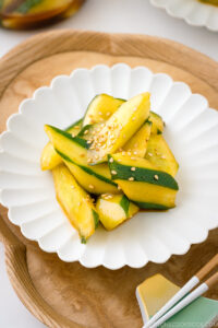 A white plate containing Spicy Japanese Pickled Cucumbers sprinkled with white sesame seeds.