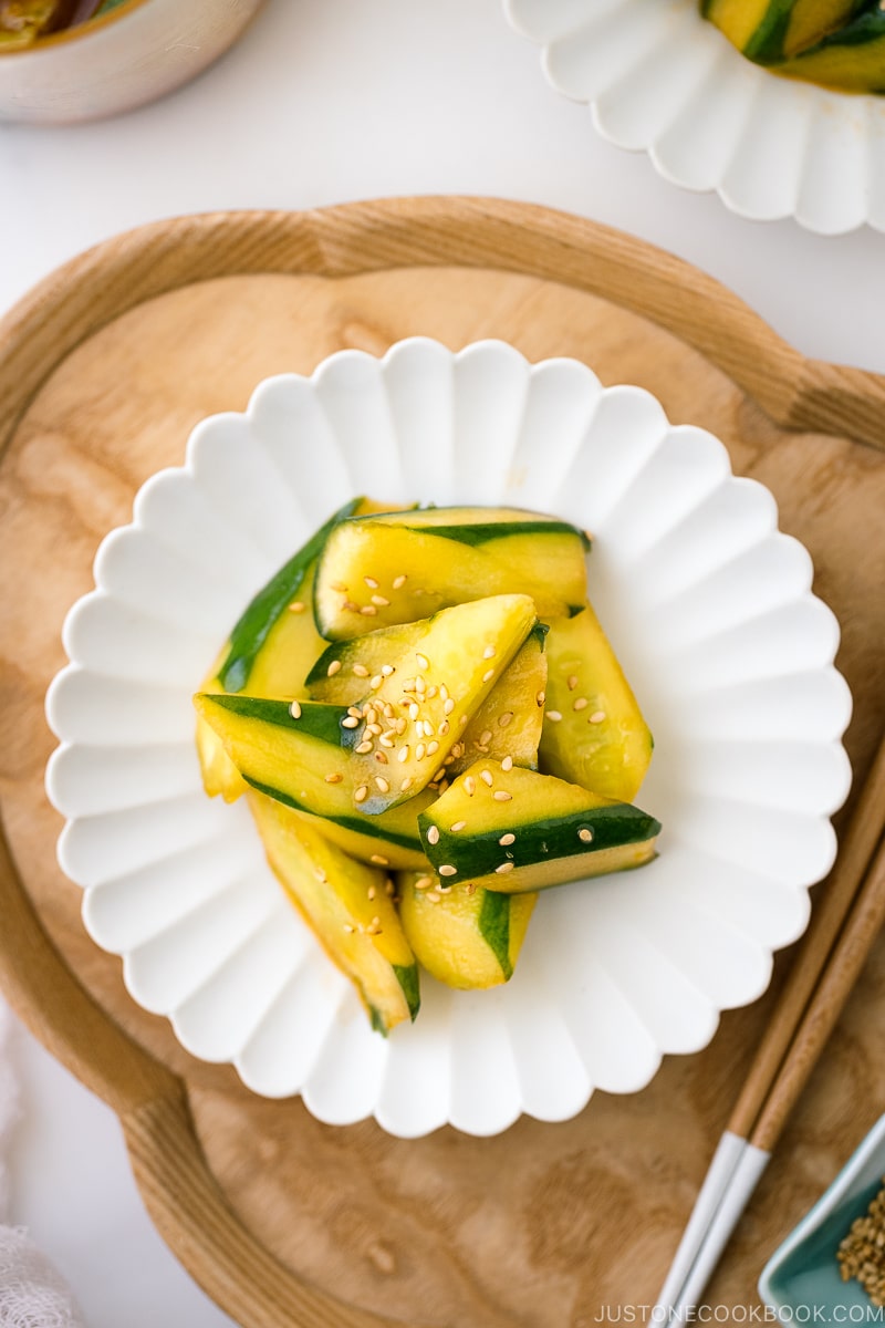 A white plate containing Spicy Japanese Pickled Cucumbers sprinkled with white sesame seeds.