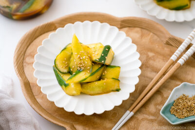 A white plate containing Spicy Japanese Pickled Cucumbers sprinkled with white sesame seeds.
