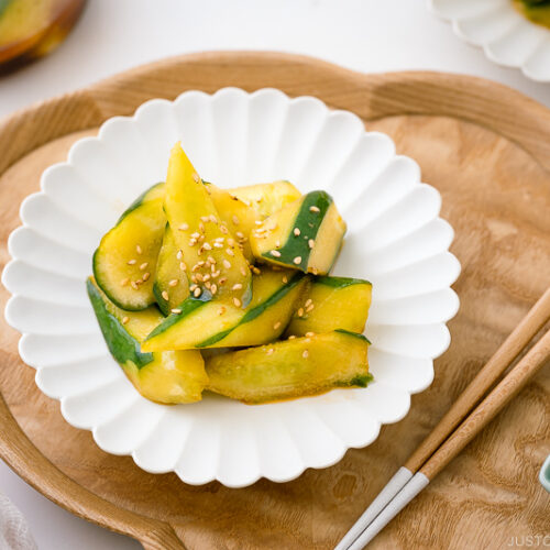 A white plate containing Spicy Japanese Pickled Cucumbers sprinkled with white sesame seeds.