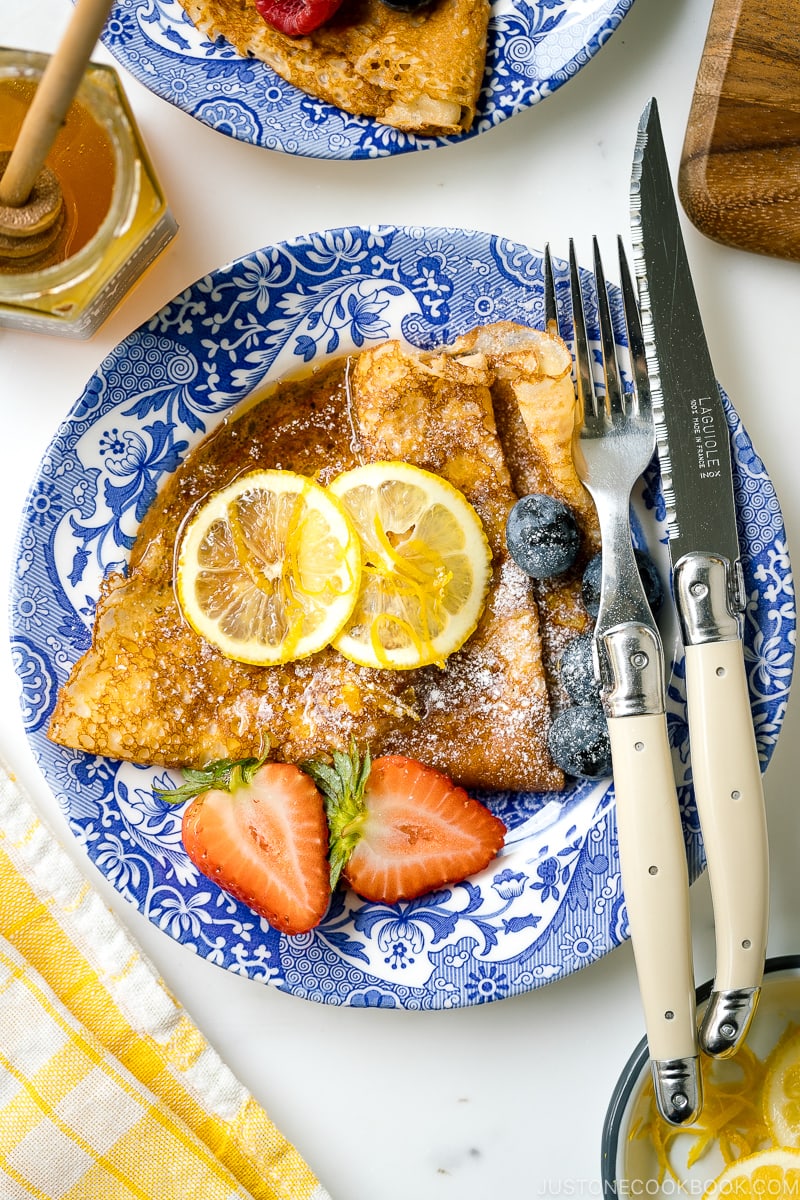 A blue plate containing lemon and sugar crepe along with fresh fruits.