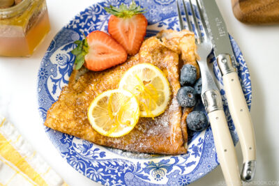 A blue plate containing lemon and sugar crepe along with fresh fruits.