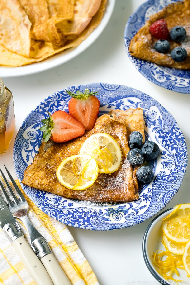 A blue plate containing lemon and sugar crepe along with fresh fruits.