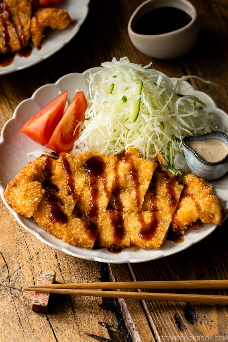 A white plate containing chicken katsu with tonkatsu sauce and shredded cabbage with sesame dressing.