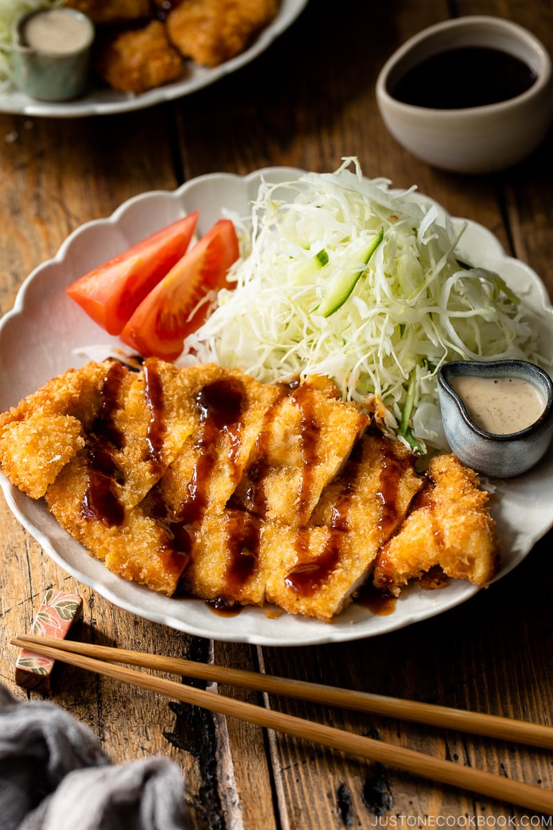 A white plate containing chicken katsu with tonkatsu sauce and shredded cabbage with sesame dressing.