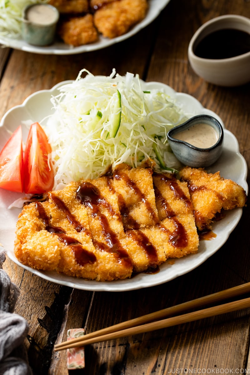 A white plate containing chicken katsu with tonkatsu sauce and shredded cabbage with sesame dressing.