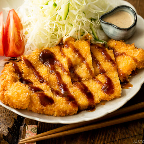 A white plate containing chicken katsu with tonkatsu sauce and shredded cabbage with sesame dressing.