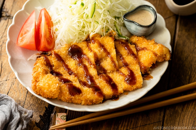 A white plate containing chicken katsu with tonkatsu sauce and shredded cabbage with sesame dressing.