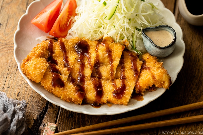 A white plate containing chicken katsu with tonkatsu sauce and shredded cabbage with sesame dressing.