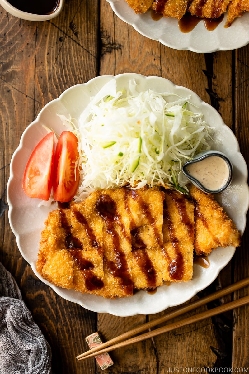 A white plate containing chicken katsu with tonkatsu sauce and shredded cabbage with sesame dressing.